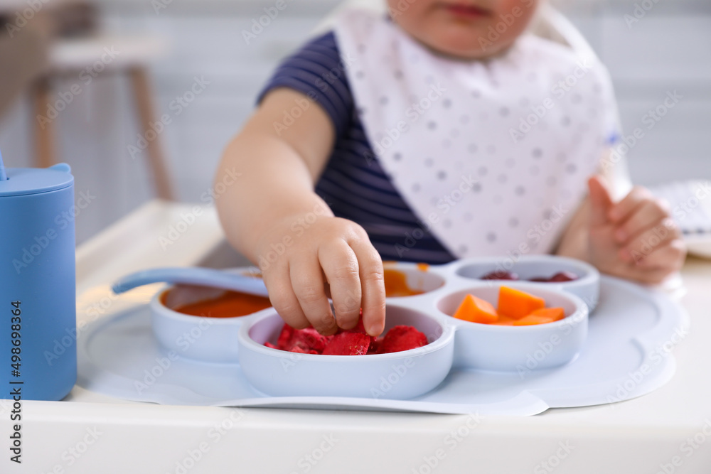 Little baby eating food in high chair at kitchen, closeup Little baby eating food in high chair at kitchen, closeup
