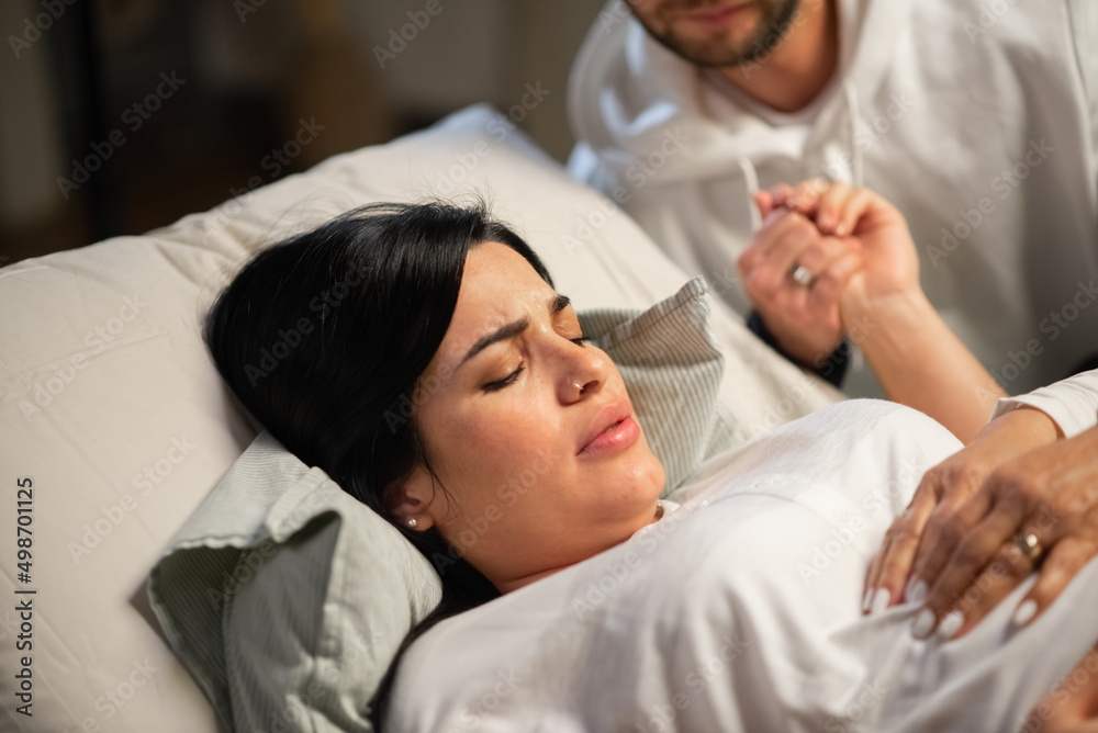 Concentrated woman giving birth at home. Woman with pierced nose lying, feeling contractions during childbirth. Pregnancy, home birth concept Concentrated woman giving birth at home. Woman with pierced nose lying, feeling contractions during childbirth. Pregnancy, home birth concept