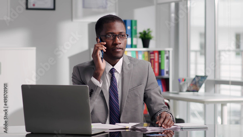 Portrait of African-American attorney advising client on smartphone and working on laptop