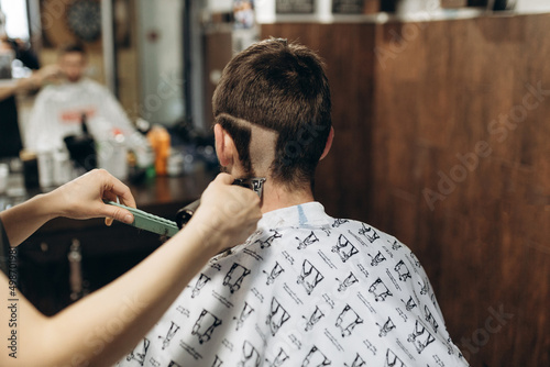 a hairdresser cuts a young guy with a hair trimmer, combing the hair on his head. Work of the master in men's haircut in a barbershop
