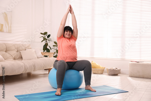 Overweight mature woman doing exercise with fitness ball at home