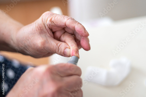 Senior Woman tests blood for glucose or sugar level for diabetes with glucometer, close up of hands, home kit for testing