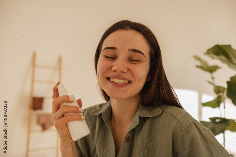 Close-up of young caucasian brunette woman holding cosmetic milk in light room. Girl closes her eyes and enjoys facial treatment. Wellness and self care concept Close-up of young caucasian brunette woman holding cosmetic milk in light room. Girl closes her eyes and enjoys facial treatment. Wellness and self care concept