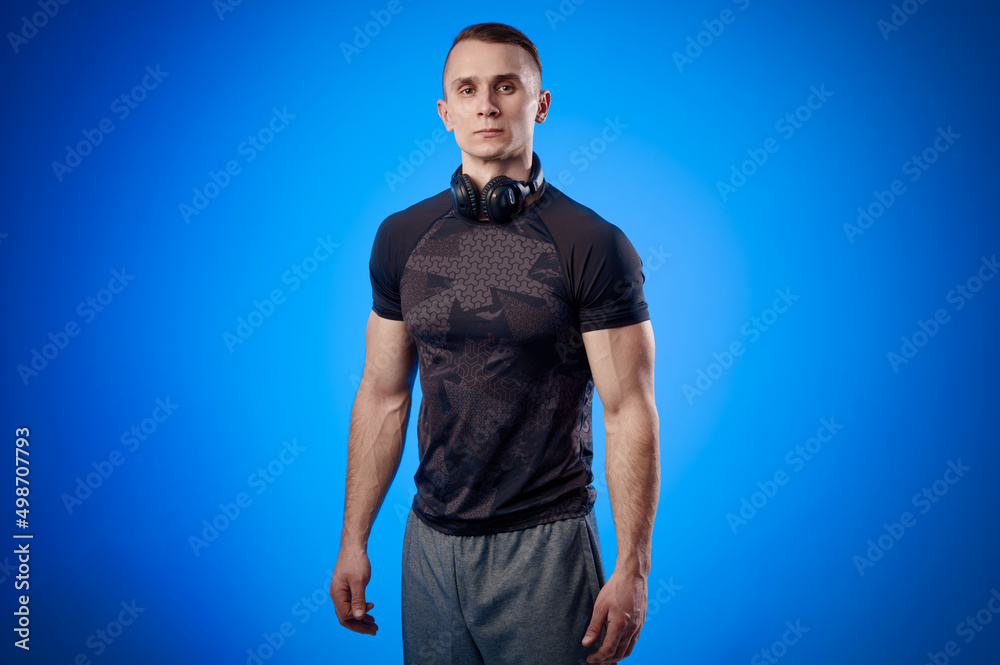 Naklejka premium Strong handsome coach with muscular body and headphones on blue isolated background