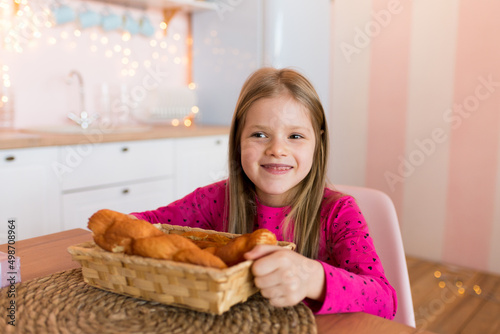 Cute smiling girl holding bread. Sits in the kitchen. 
