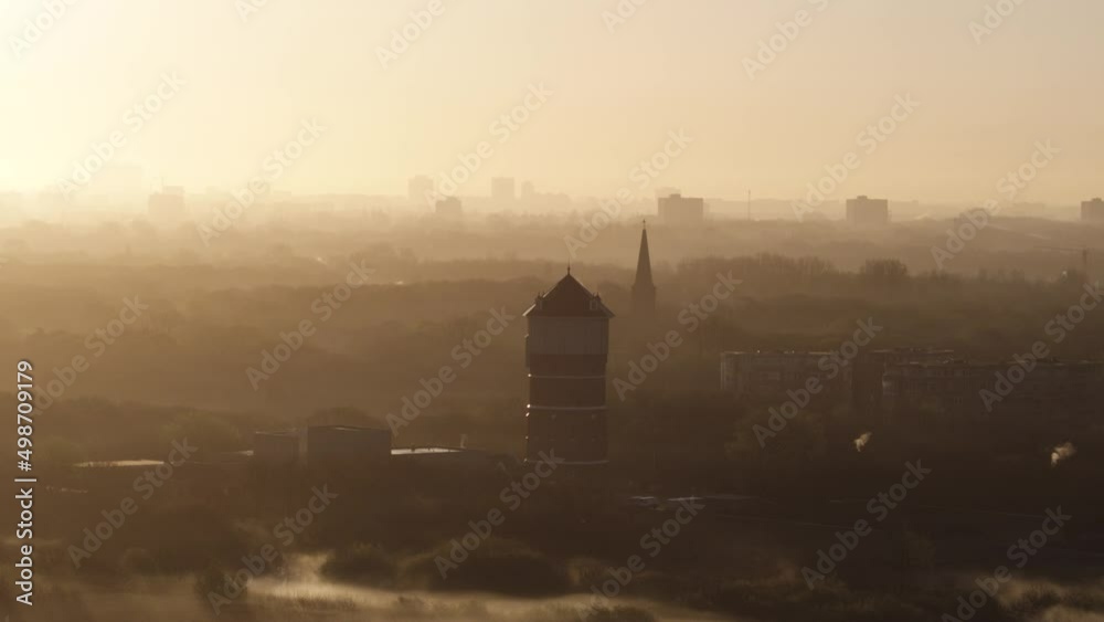 Aerial orbiting shot of the Monster water tower near the dunes of kijkduin, with the city of Den Haag (The Hague) in the background on a bright foggy and misty morning with golden light Aerial orbiting shot of the Monster water tower near the dunes of kijkduin, with the city of Den Haag (The Hague) in the background on a bright foggy and misty morning with golden light