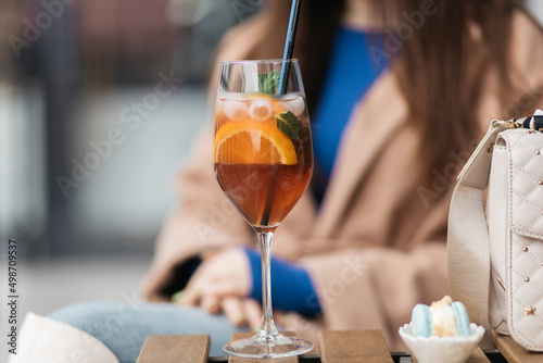 Young girl holding an aperol spritz. Aperol cocktail syringe in a glass. Young girl in a restaurant with a glass on a black background.