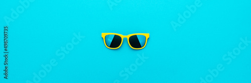 Flat lay image of vivid color plastic sunglasses on turquoise blue background with copy space. Minimalist photo of stylish yellow sunglasses as summer concept.