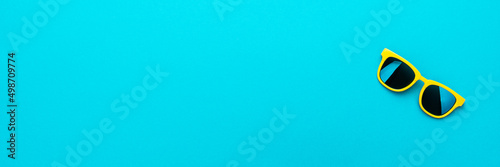 Minimalist photo of stylish yellow sunglasses as summer concept. Close-up image of vivid color plastic sunglasses on turquoise blue background with copy space.