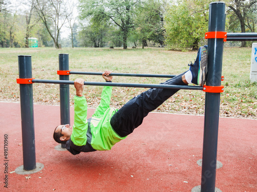 Athlete young man doing exercise at the outdoor gym. Fit male with glasses working out exercising. Casual sportswear. Healthy lifestyle concept. 