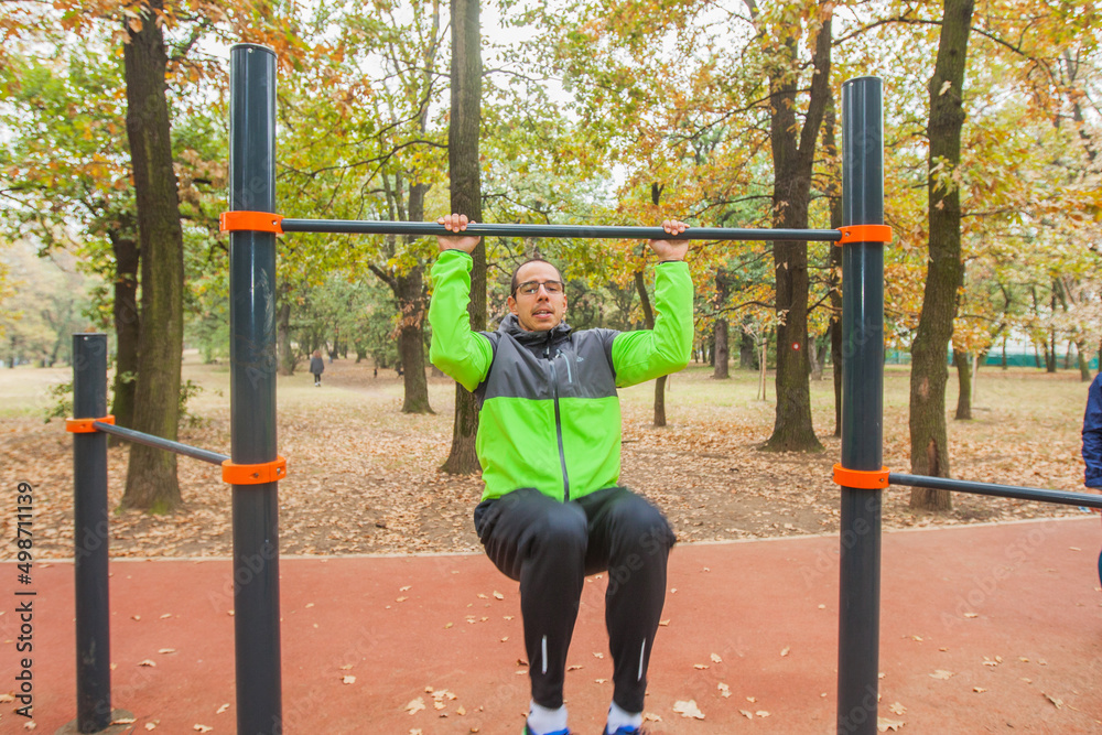 Sporty young man doing pull-ups exercise at the outdoor gym. Male athlete training outside. Fitness man exercising. Casual sportswear. Healthy lifestyle concept. 