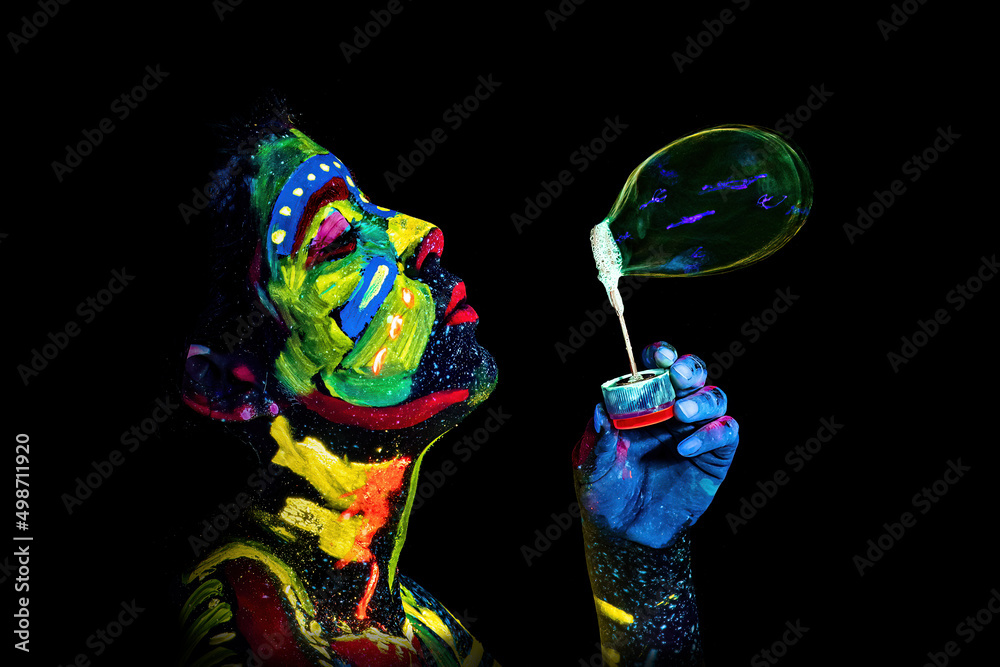 Girl painted with UV colors blows a soap bubble