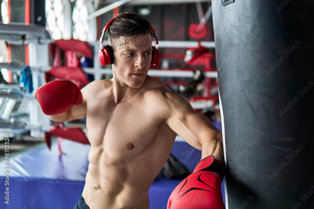 Young athlete fitness man with boxing gloves doing kick boxing training in sport gym.