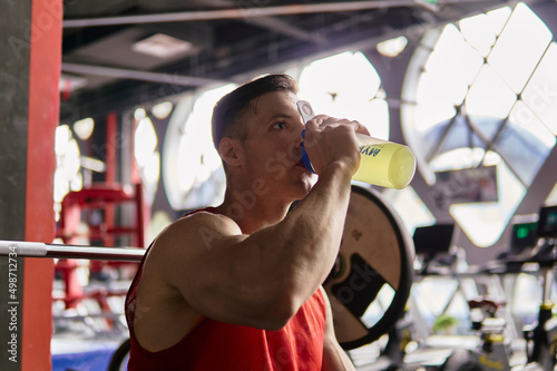 Muscular man drinking energy drink in gym.