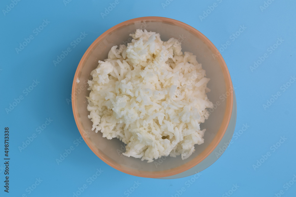 Cooked white rice in a plastic bowl isolated on a blue background Cooked white rice in a plastic bowl isolated on a blue background
