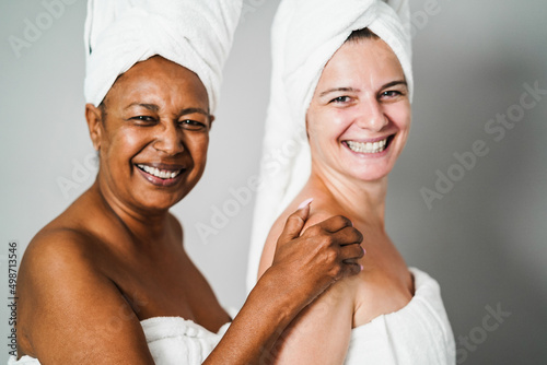 Multiracial senior women with diverse skin and body laughing together while wearing body towels - Focus on left female hand