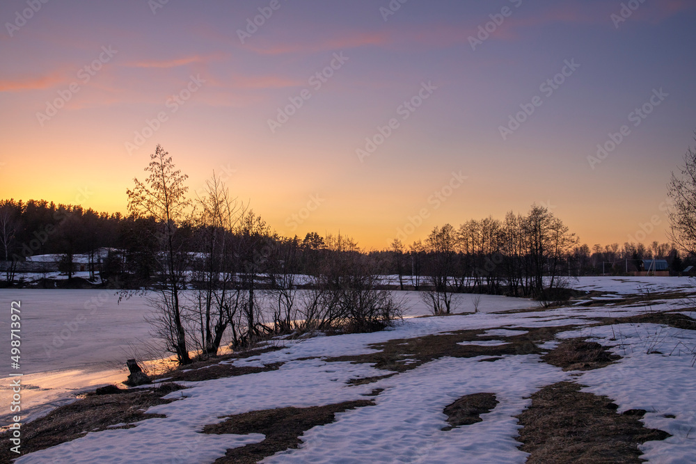 Evening spring landscape, trees by the river, snow and thawed patches. Charming landscape in early spring against the backdrop of sunset. Melting ice and snow. Evening spring landscape, trees by the river, snow and thawed patches. Charming landscape in early spring against the backdrop of sunset. Melting ice and snow.
