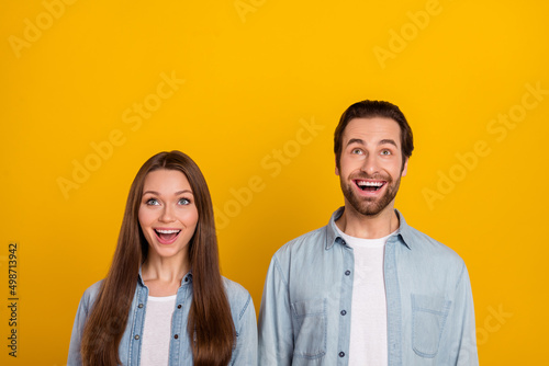 Photo of funny impressed husband wife wear jeans shirts looking up empty space isolated yellow color background