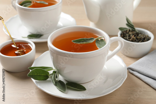 Cup of aromatic sage tea served with honey on wooden table