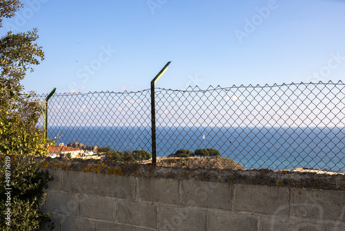 Fence made of concrete and mesh behind whom you can see the sea. Metal mesh, chain-link, against the background of the sea.