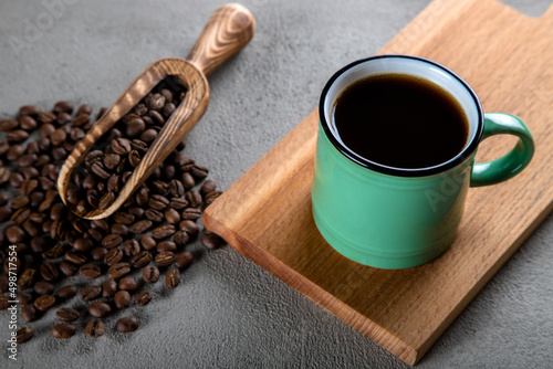 Green cup of coffee with coffee beans on wooden background