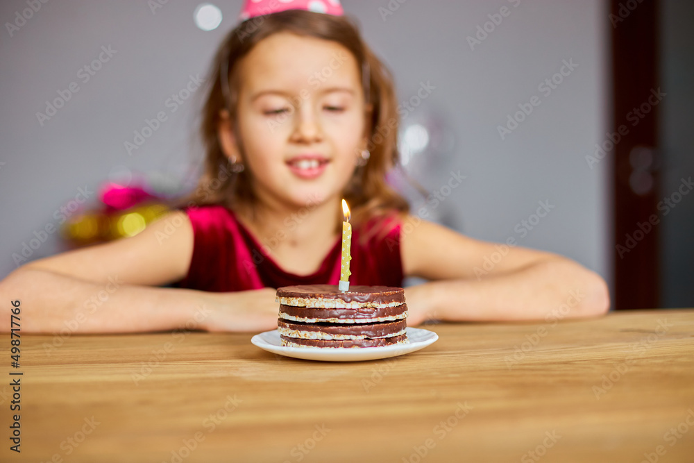 A little girl is wearing a birthday hat makes a wish , looking at a Birthday Cake A little girl is wearing a birthday hat makes a wish , looking at a Birthday Cake