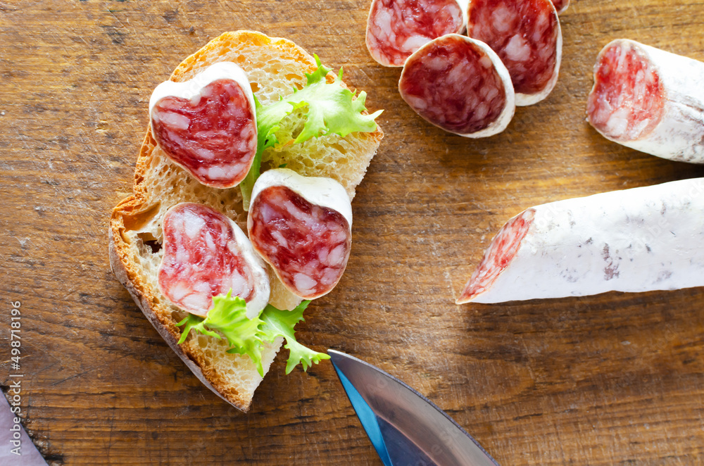 Sandwich with Catalan thin sausage with mold - fuet, on a wooden cutting board. Horizontal orientation. Top view. Sandwich with Catalan thin sausage with mold - fuet, on a wooden cutting board. Horizontal orientation. Top view.