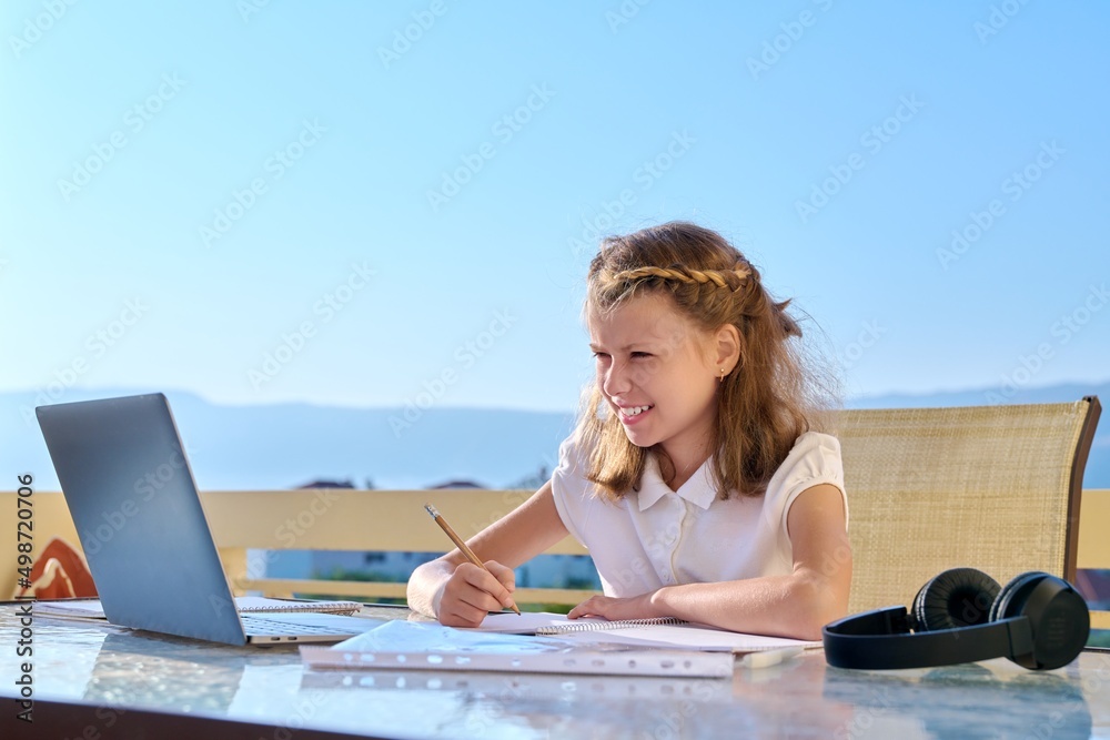 Girl child with headphones is studying using a laptop.