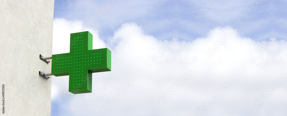 Green shining medical cross indicating the location of a pharmacy on street. Banner medical cross on sky background