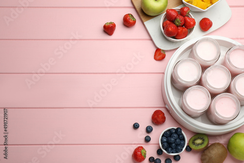 Modern yogurt maker with full jars and different fruits on pink wooden table, flat lay. Space for text