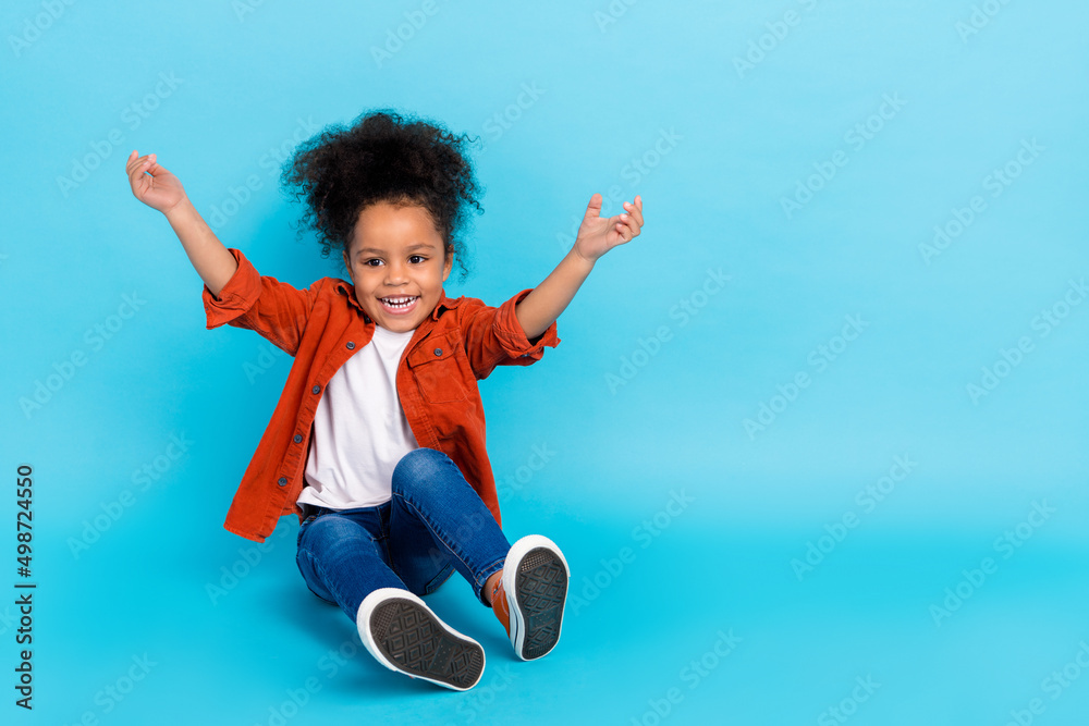 Full length photo of cute curly little girl wear shirt jeans footwear isolated on blue background