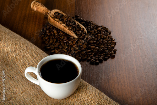 White cup of coffee with coffee beans on wooden background