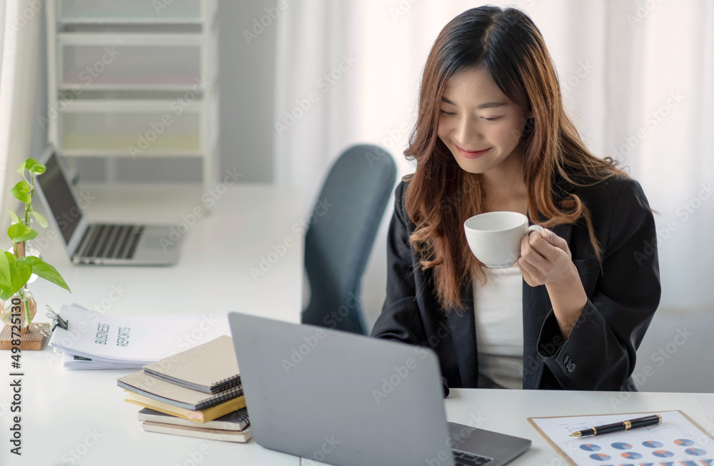 Smiling Asian businesswoman holding a coffee mug and laptop at the office. Smiling Asian businesswoman holding a coffee mug and laptop at the office.