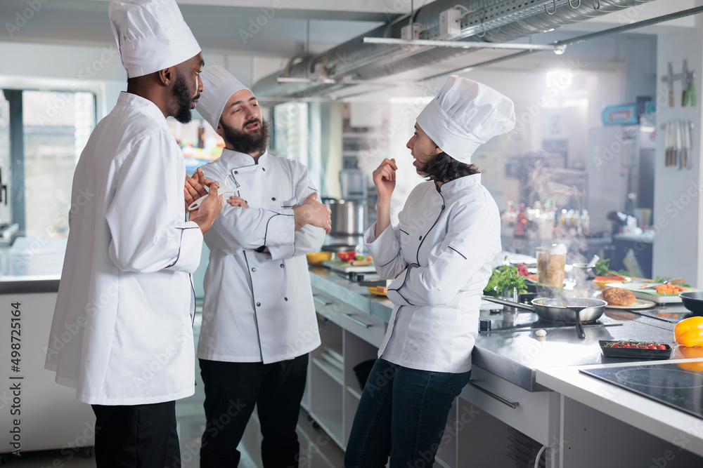 Professional food industry workers brainstorming lunch meal ideas while standing in kitchen. Multiethnic gastronomy experts planning dinner service menu while discussing about what ingredients to use.
