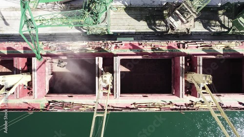 Loading dry cargo ship of wheat by cranes in port. Top down view loading into holds of sea cargo vessel
