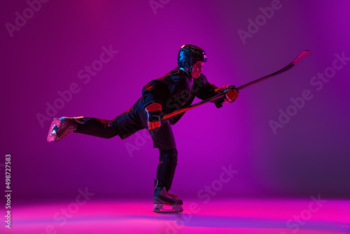 Canvas Print Portrait of boy, child, hockey player training, practising isolated over purple background in neon light