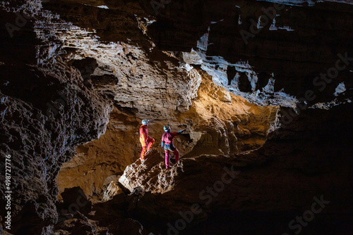 Two cavers - girl and boy are looking through the cave gallery; speleology photo