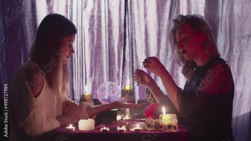 Female fortune teller uses a magic pendulum on client hand and reading palm lines
