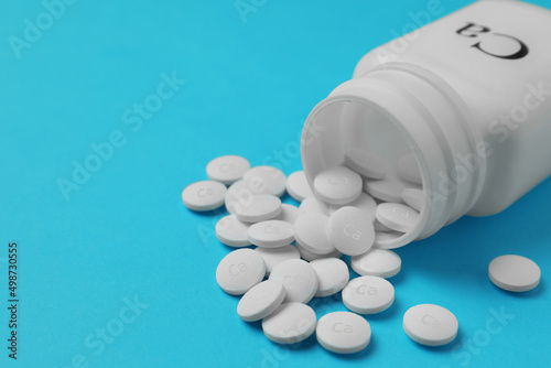Overturned bottle of calcium supplement pills on light blue background, closeup. Space for text