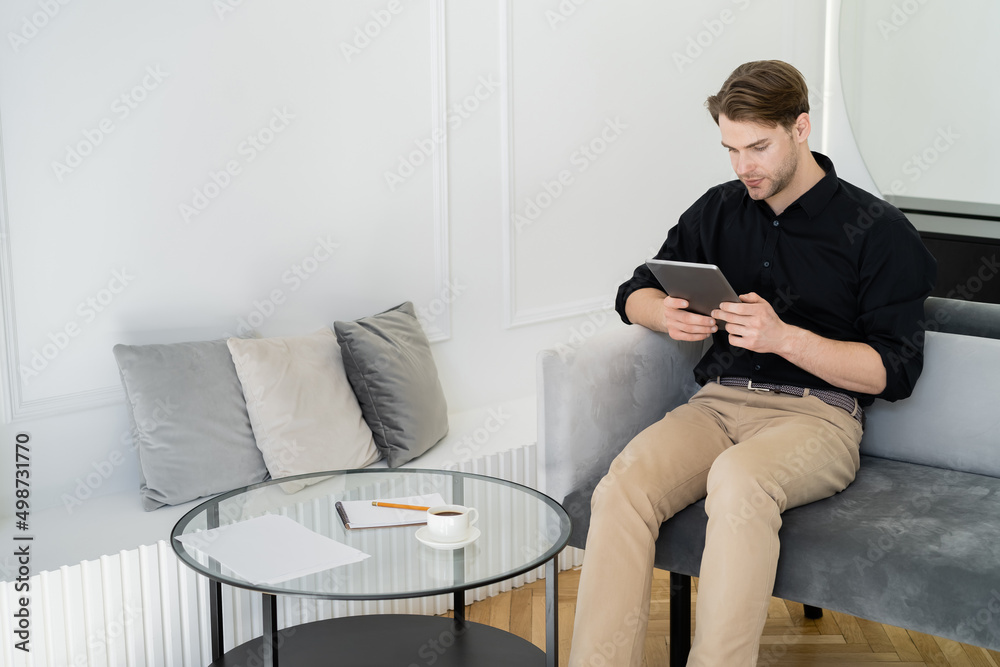 young man using digital tablet near coffee table in living room.