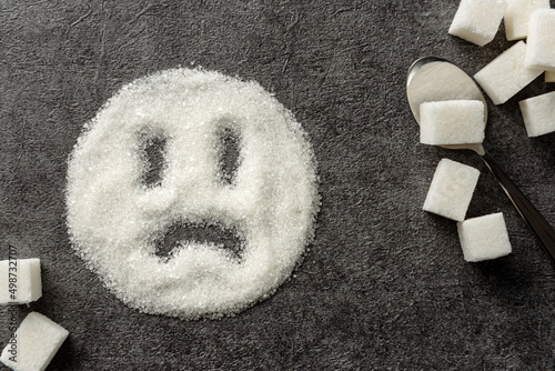 A sad smiley drawn on a pile of sugar. Sugar harm concept.
