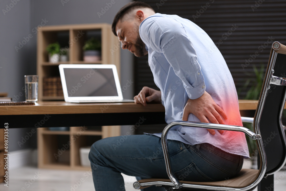 Man suffering from back pain while working with laptop in office. Symptom of poor posture - obrazy, fototapety, plakaty 