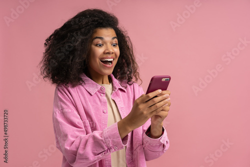 Φωτογραφία Excited African American woman holding smartphone playing mobile game isolated on pink background