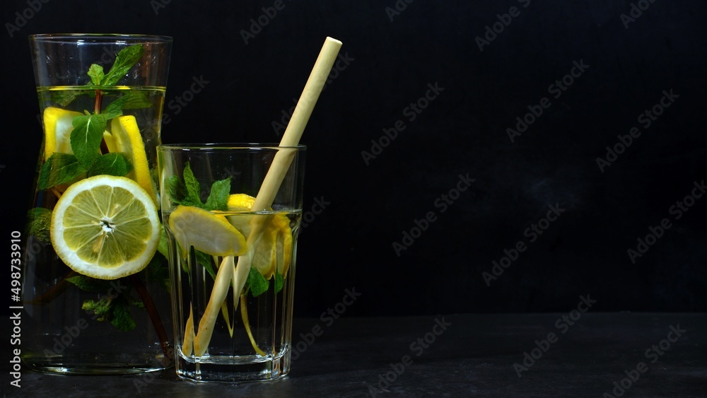 Fototapeta premium Water carafe with lemon and mint and bamboo straw against dark background