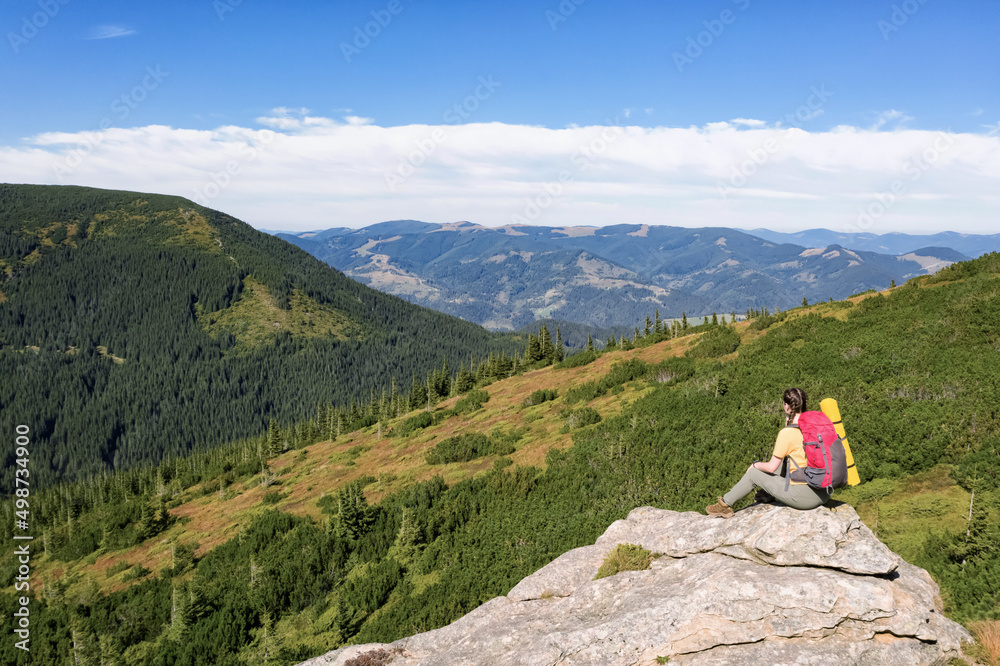 Woman with backpack and sleeping mat on rocky cliff in mountains, back view