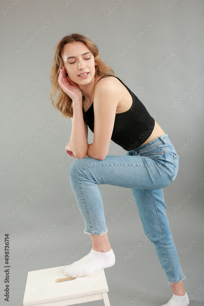 Beautiful girl model appearance in light jeans and black T-shirt on a gray studio background. Girl model sitting on a white chair. Beautiful blonde shows poses for a photo shoot
Beautiful girl model appearance in light jeans and black T-shirt on a gray studio background. Girl model sitting on a white chair. Beautiful blonde shows poses for a photo shoot