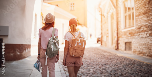 Two woman with backpacks walking in the old Tallinn, Estonia.