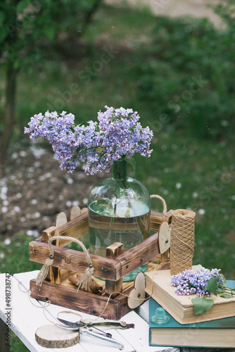 A beautiful postcard. Old books, a wooden box, a garden pruner and a bouquet of purple lilac. Still-life. Spring. Processing in the style of an old film.