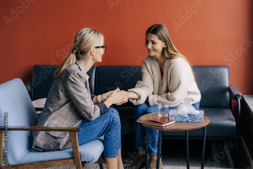 Empathic female psychologist holding female client's hand giving mental professional support photo