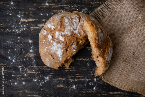 Broken loaf of homemade bread on rustic napkin on dark background